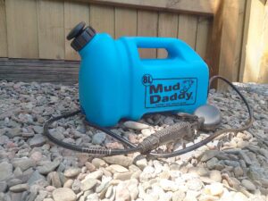 a blue 8l mud daddy photographed on gravel with a wooden fence background